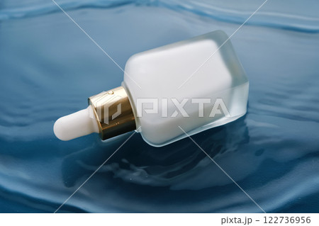 Bottle with white moisturizing serum in water on blue background. 122736956