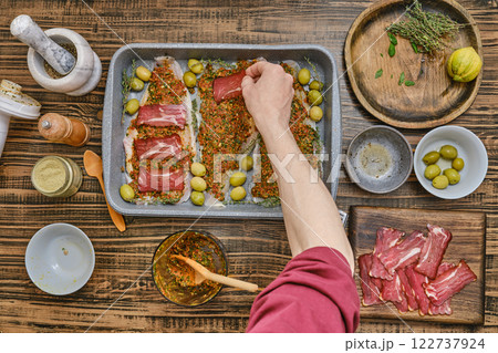 Hand places slices of bacon atop a seasoned fish fillets on a baking tray Hand places slices of bacon atop a seasoned fish fillets on a baking tray 122737924