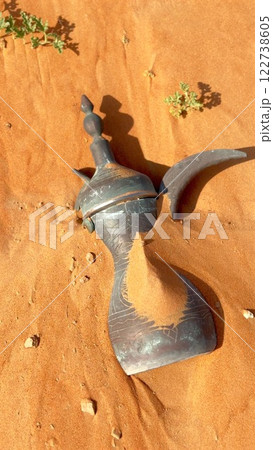 Desert coffee pot rests on grains of sunlit sand, preserving cultural heritage. This pot connects generations through coffee traditions in desert communities and history Arabic Dallah, pot 122738605