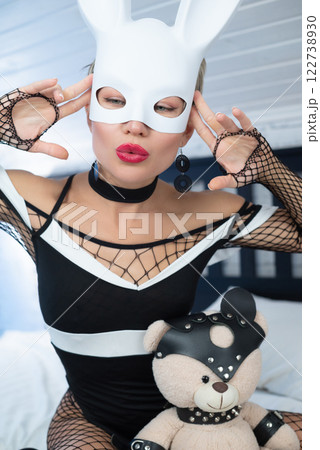 Sexy girl in black dress and a white rabbit mask from a sex shop poses erotically seducing on the bed 122738930