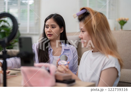 Beauty broker discussing makeup techniques with a friend during a live broadcast, showcasing collaboration and beauty tips. 122739316