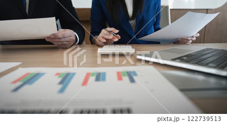 Close-up of a diverse business team reviewing financial documents and calculating data in a modern office environment. 122739513