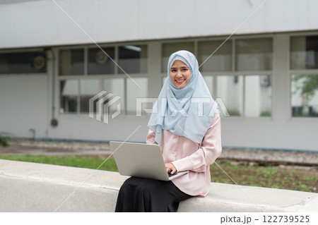 Muslim businesswoman in hijab smiling while working on a laptop outdoors. 122739525