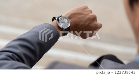 Close up of a young Asian businessman checking his watch in a modern outdoor business environment. Close up of a young Asian businessman checking his watch in a modern outdoor business environment. 122739543