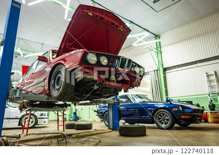 In a fully equipped automotive workshop environment, there are two classic cars being carefully serviced 122740118