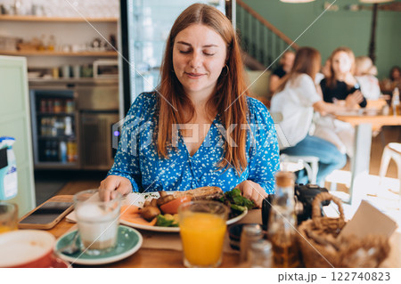 Happy 30s female wearing stylish outfit eating delicious breakfast including eggs and grilled mushrooms, salmon, avocado served on wooden table. Food concept Happy 30s female wearing stylish outfit eating delicious breakfast including eggs and grilled mushrooms, salmon, avocado served on wooden table. Food concept 122740823