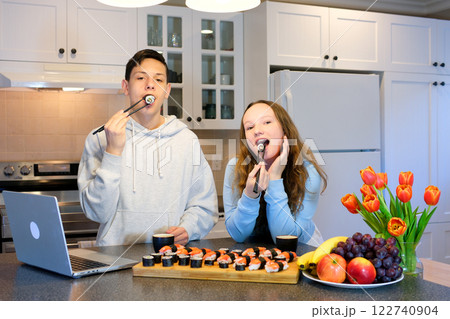 Young excited amazed cool fun woman 20s in casual clothes hold in hand eat makizushi sushi roll served on black plate traditional japanese food chopsticks isolated on plain pastel pink background. 122740904