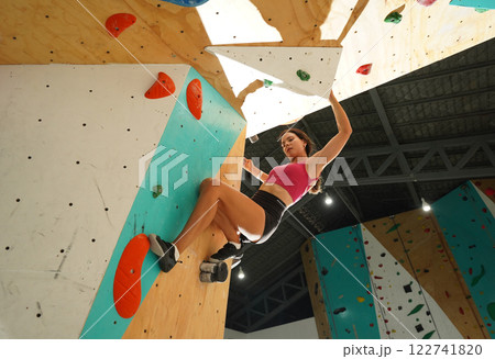 A strong female climber climbs an artificial wall with colorful grips 122741820