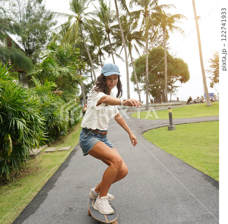 A young woman is skillfully riding a skateboard down a scenic park A young woman is skillfully riding a skateboard down a scenic park 122741933