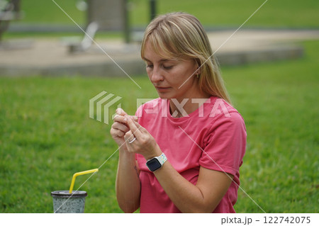 Young woman beading colorful bracelets outdoors in a park Young woman beading colorful bracelets outdoors in a park 122742075
