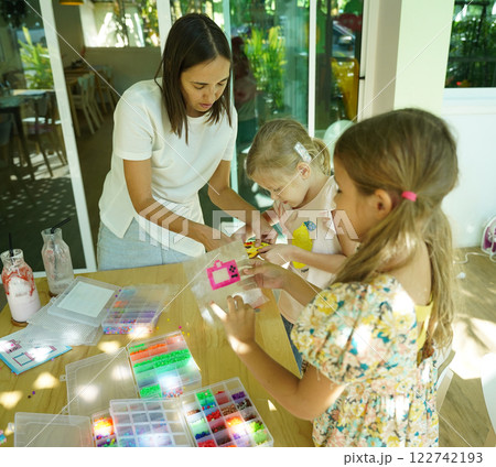 Teacher in workshop teched two girls how to assemble a thermo mosaic  122742193