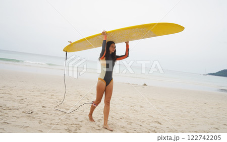 Young woman wearing tight wetsuit is going to surfboard at beautiful beach 122742205