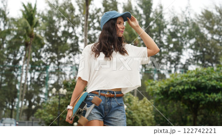 A woman is walking at the city park while carrying a skateboard in her hands A woman is walking at the city park while carrying a skateboard in her hands 122742221