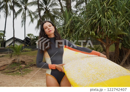 Young woman wearing tight wetsuit is going to surfboard at beautiful beach 122742407