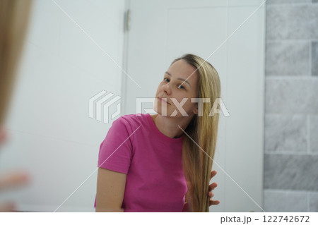 A woman is expertly styling her hair using a blow dryer and brush while in the bathroom A woman is expertly styling her hair using a blow dryer and brush while in the bathroom 122742672