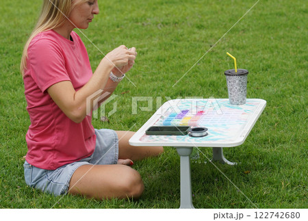 Young woman beading colorful bracelets outdoors in a park Young woman beading colorful bracelets outdoors in a park 122742680
