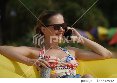 A young woman on the beach lounging on a yellow bean bag  122742942