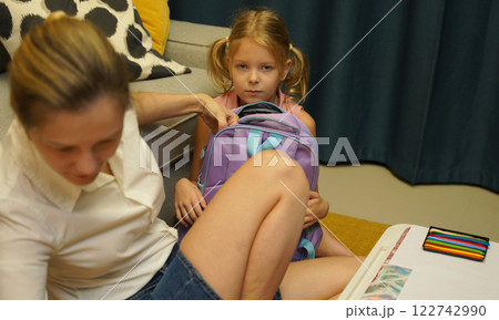 Mother helps her daughter pack her backpack Mother helps her daughter pack her backpack 122742990