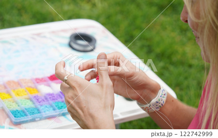 Young woman beading colorful bracelets outdoors in a park 122742999