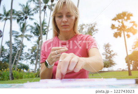 Young woman beading colorful bracelets outdoors in a park 122743023