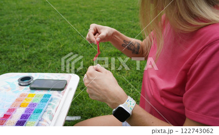 Young woman beading colorful bracelets outdoors in a park 122743062