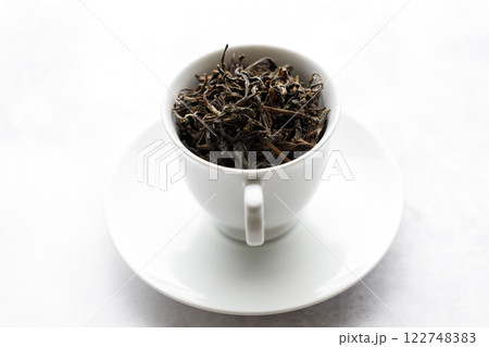 Cup of hot tea filled with tea leaf on white table background. Cup of hot tea filled with tea leaf on white table background. 122748383