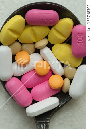 A lot of pills of different colors and shapes stacked together on metal spoon with white background. A lot of pills of different colors and shapes stacked together on metal spoon with white background. 122748500