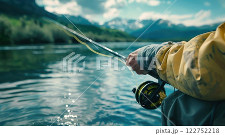Fisherman Mid-Cast by Tranquil Lake with Mountain Backdrop for Outdoor Adventure and Recreation 122752218