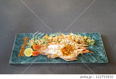 Lobster Pad Thai is served with yellow noodle, fried tofu, cress, bean sprouts, chilli power, garlic chives, and lime put on a rectangular plate. 122753910