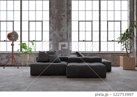 Industrial loft with large windows, dark sofa, and plants. 122753997