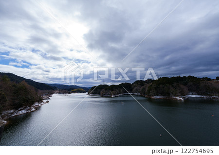 雪景色の奈良布目ダム　鉛色の雲に覆われ暗くなっていく布目湖の上空と雲間から覗く青空を映す湖面 122754695