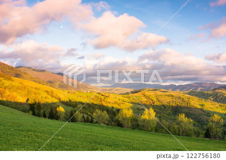 mountain landscape in spring. trees behind green meadow at sunset. countryside scenery with rolling hills. sky with clouds in evening light picturesque destination for outdoor adventure mountain landscape in spring. trees behind green meadow at sunset. countryside scenery with rolling hills. sky with clouds in evening light picturesque destination for outdoor adventure 122756180