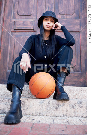 Basketball, fashion and model influencer of a woman posing on steps in an urban city with fashionable style. Female portrait of trendy, stylish and cool person in sports promotion for ball game. 122756513