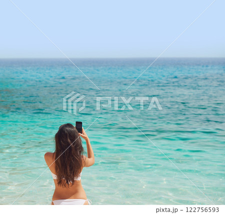 Woman, bikini and phone by ocean in back view for social media, post or profile picture of tropical vacation. Female person, mobile or holiday for travel, island or Hawaii for wellness, care or relax Woman, bikini and phone by ocean in back view for social media, post or profile picture of tropical vacation. Female person, mobile or holiday for travel, island or Hawaii for wellness, care or relax 122756593