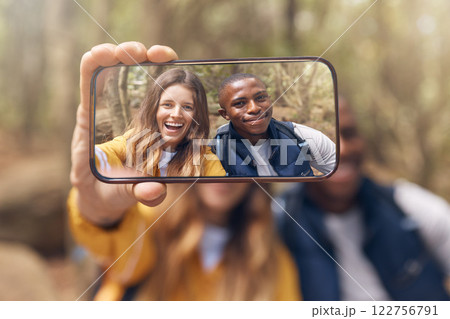 Happy couple taking a selfie on a phone while in nature on a romantic date in the forest. Multiracial, love and traveling man and woman taking picture with smartphone camera after hiking in the woods 122756791