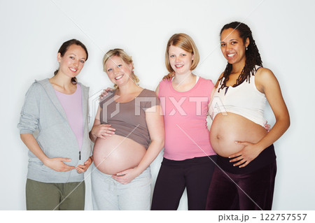 Pregnant, mother and friends with women in studio against a white background feeling happy with a smile. Pregnancy, health and wellness with positive female parents holding their abdomen together 122757557