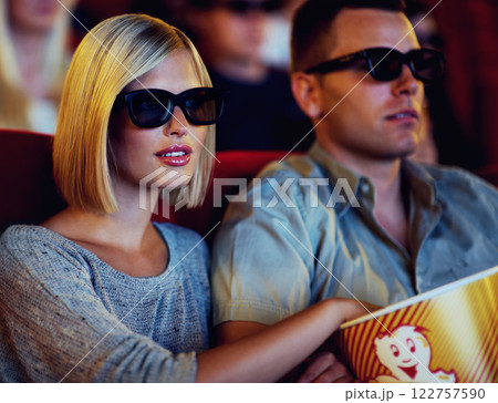Couple, 3D movie and cinema of a man and woman sitting and eating popcorn together wearing glasses. People in a relationship watching a film in a theatre for indoor entertainment while having snacks. 122757590