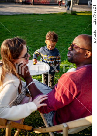 Happy Family, Mother and Father With Child Enjoying Quality Time Together, Relaxing On Lounge Chairs On Grass In Park On Warm And Sunny Day. 122758221