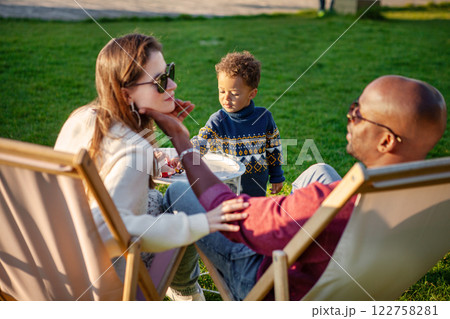 Happy Family holiday, Mother and Father With Child Enjoying Quality Time Together, Relaxing On Lounge Chairs On green Grass In Park On Warm And Sunny Day. Happy Family holiday, Mother and Father With Child Enjoying Quality Time Together, Relaxing On Lounge Chairs On green Grass In Park On Warm And Sunny Day. 122758281
