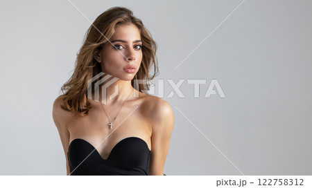 Portrait Beautiful Young Woman With Long Wavy Hair Wearing Black Strapless Dress, Looking Camera On Light Background. Brunette European Fashion model in studio, beauty, smooth skin and modern style 122758312