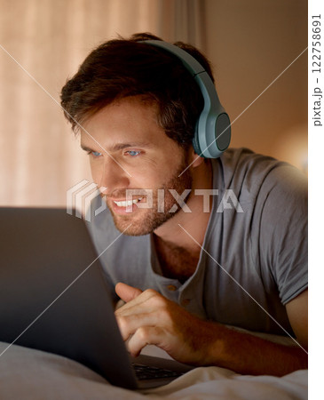 Laptop, online tv and movie subscription with headphones late at night in his bedroom. Man with insomnia distracted with steaming internet to watch film, esports or enjoy gaming to relax at home 122758691
