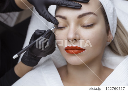 Permanent makeup. Cosmetologist tattoo artist applies a contour to the client's eyelid for subsequent application of eye tattooing 122760527
