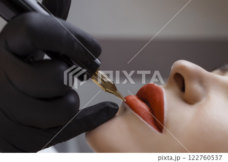 Cosmetologist makes permanent makeup on a woman's face. Specialist applies a tattoo on the patient's lips close-up 122760537