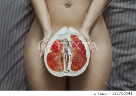 A naked girl holds a grapefruit symbol of the vagina in her hands. Intimate rejuvenation and epilation of the bikini area 122760541