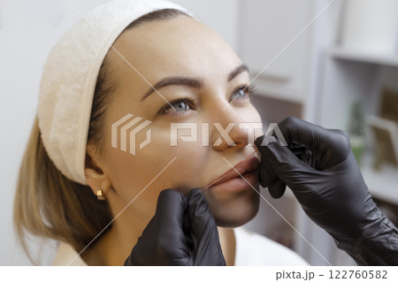 Young woman with permanent makeup on her lips in a cosmetologists salon. Permanent makeup tattoo. draw a line with a red lip thread 122760582