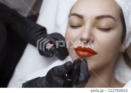 Cosmetologist makes permanent makeup on a woman's face. Specialist applies a tattoo on the patient's lips close-up 122760603