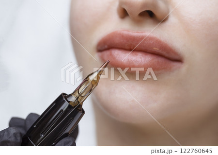 Cosmetologist makes permanent makeup on a woman's face. Specialist applies a tattoo on the patient's lips close-up 122760645
