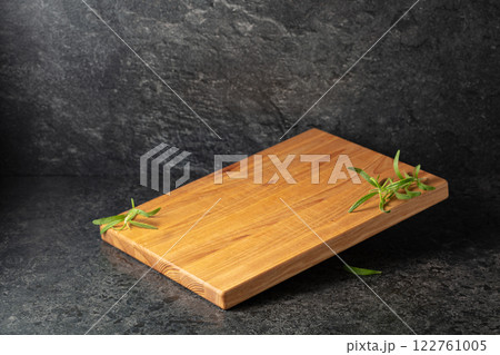 Empty cutting board with rosemary on a black stone background. 122761005