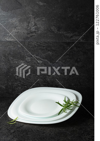 Empty white plates with rosemary on a black stone background. 122761006