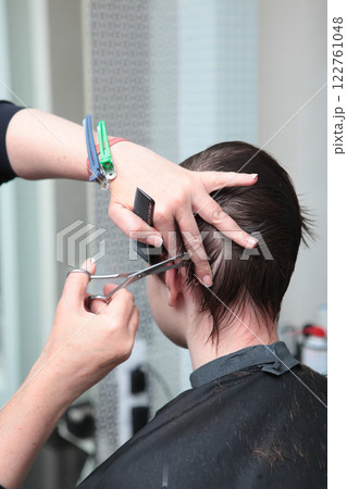 Barbershop. Close-up of man's haircut. Master of barbershop makes haircut with scissors. Giving the haircut perfect shape. Vertical photo. 122761048